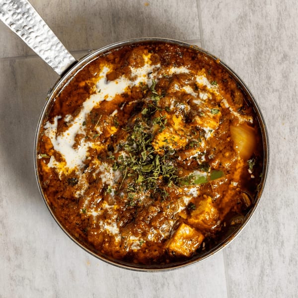 A close-up, top-down view of a pan of paneer butter masala, garnished with cream and herbs.