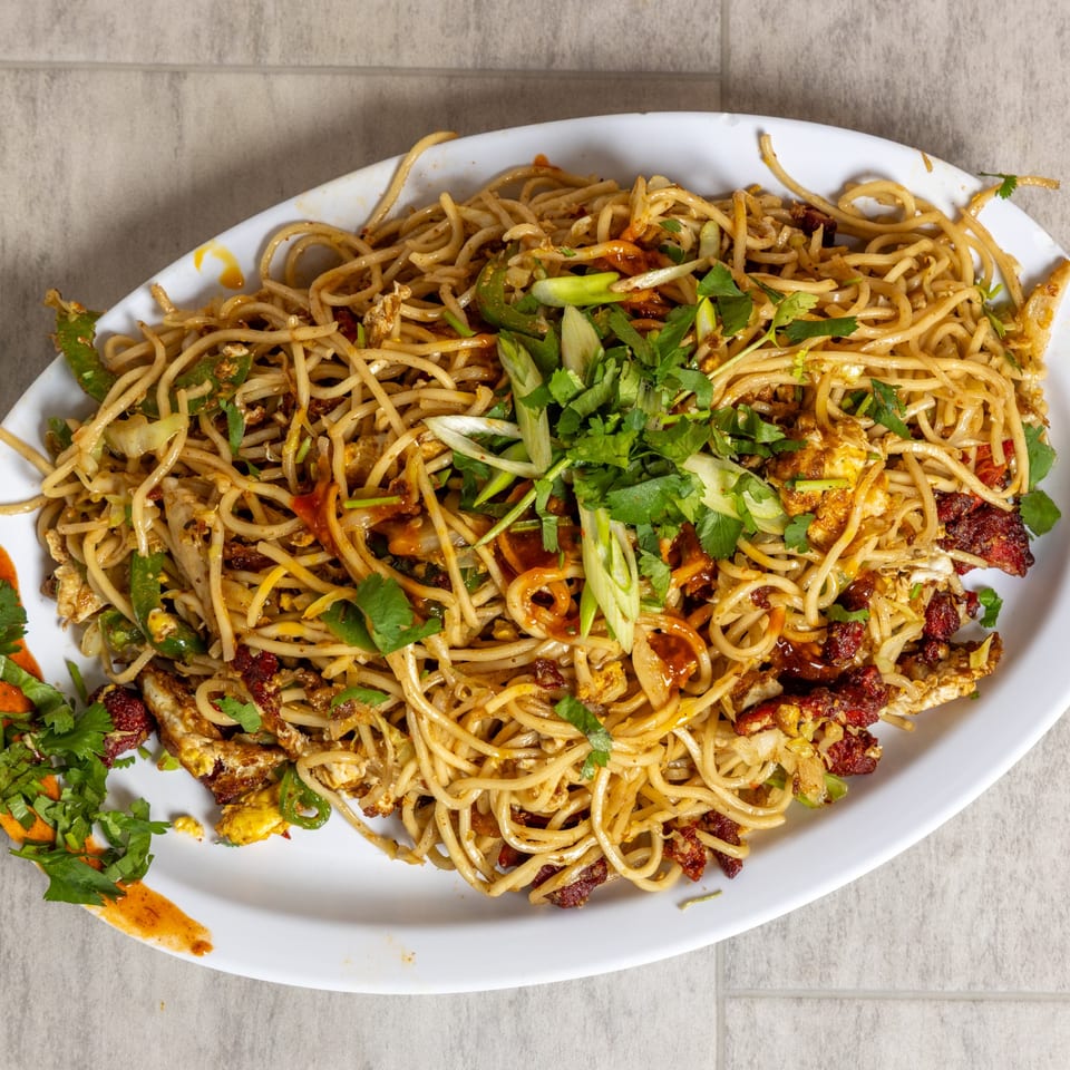 A large white platter filled with stir-fried noodles, garnished with green onions and cilantro.
